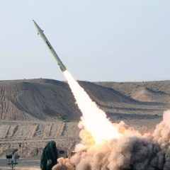 "A ballistic missile launching into the sky from a desert terrain with thick smoke clouds, representing Iran's missile capabilities."