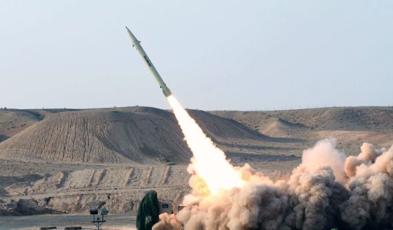 "A ballistic missile launching into the sky from a desert terrain with thick smoke clouds, representing Iran's missile capabilities."