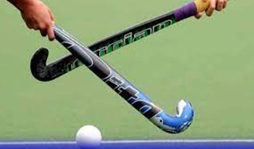 A close-up shot from the file hockey-1.jpg showing two players' hands holding field hockey sticks that are crossed in an "X" shape over a white ball on a green artificial turf.